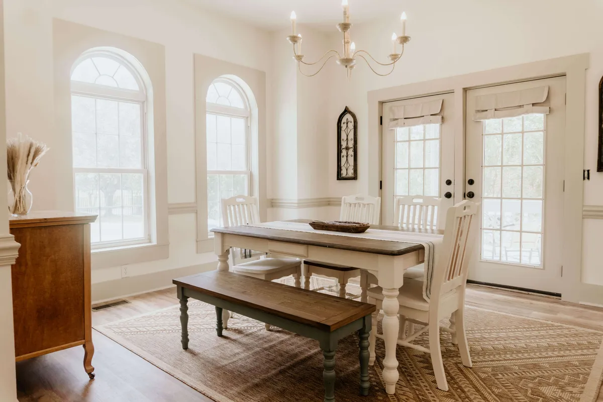 The dining area is highlighted here, centered around a large dining table under an elegant chandelier. Arched windows allow warm natural light to fill the space, while a built-in bench adds a cozy, communal touch. The setting is ready for both formal dinners and relaxed breakfasts.