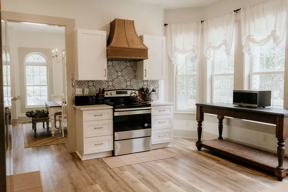A stylish kitchen scene featuring modern appliances, a decorative range hood, and large windows that bathe the space in natural light. The room exudes an inviting, cozy atmosphere perfect for cooking, entertaining, and gathering with loved ones.