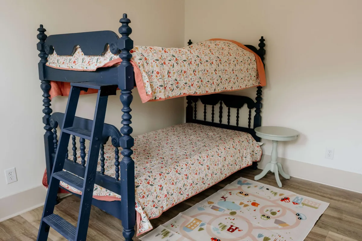 A playful and inviting children's bedroom featuring colorful bunk beds, lively bedding, a whimsical rug, and a small side table. The room is designed for both comfort and imaginative play, creating a welcoming sanctuary for young dreamers.