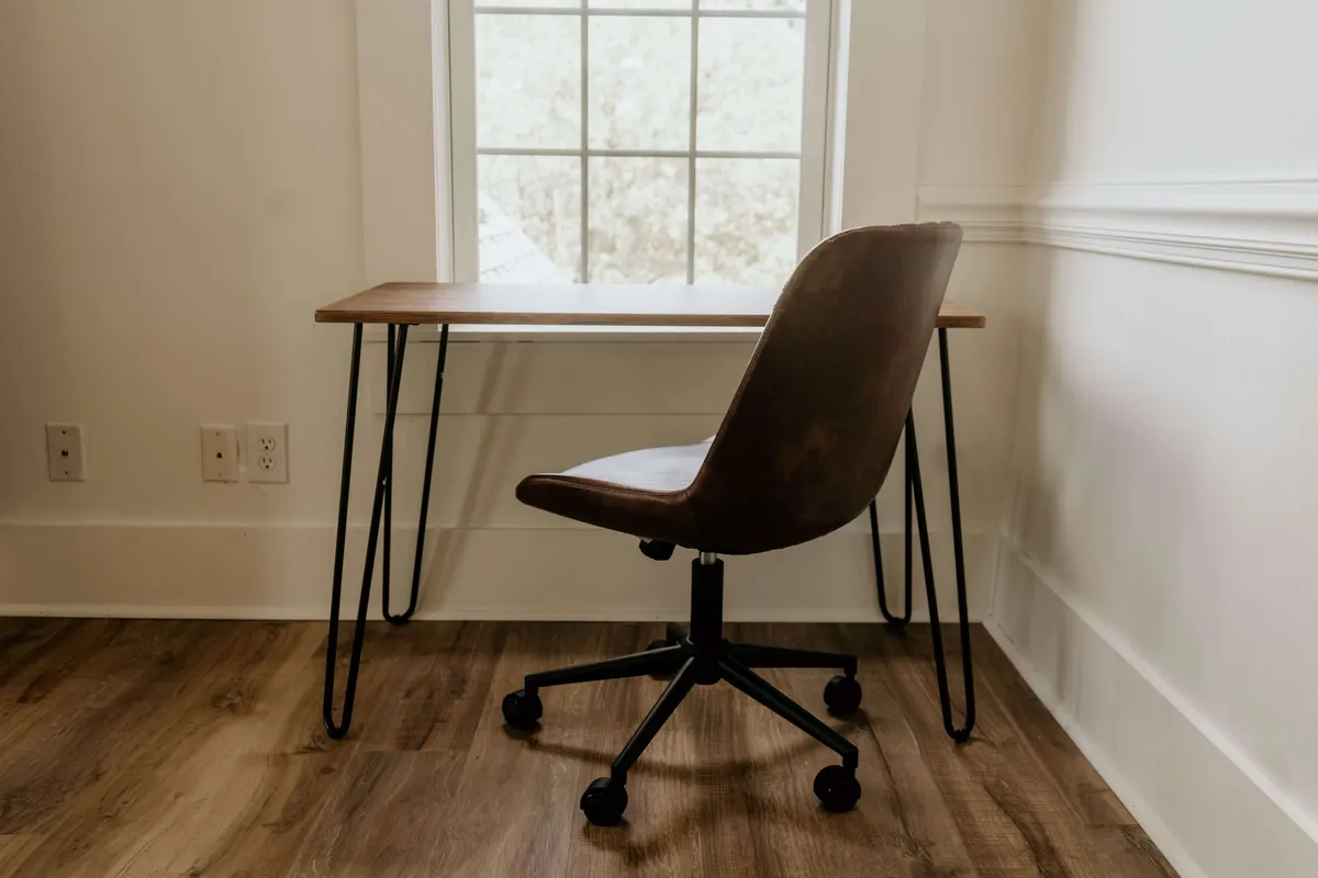 A modern wooden desk and sleek chair positioned in front of a large window, where daylight streams in, creating a tranquil workspace. This area is perfectly suited for reading or quiet study, with the window framing an inspiring view.