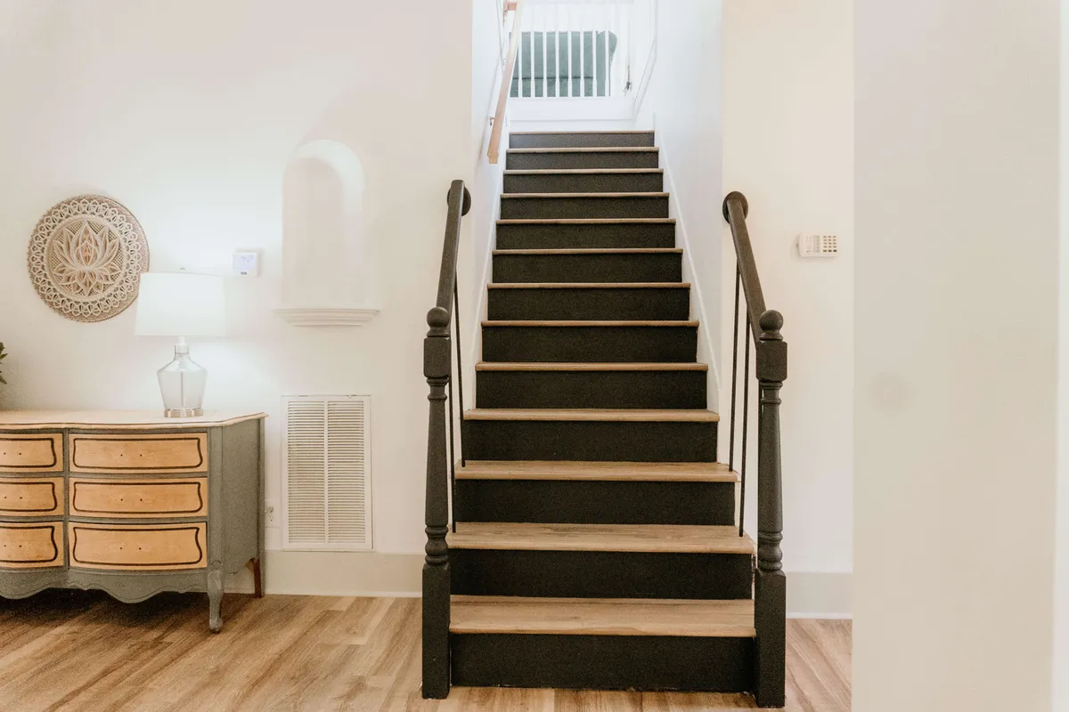 A bright and inviting entryway with a staircase adorned with holiday decorations, a console table, a lamp, and tasteful wall art. The space feels welcoming and suggests the first steps into a home where families reunite and prepare for a day of fun.