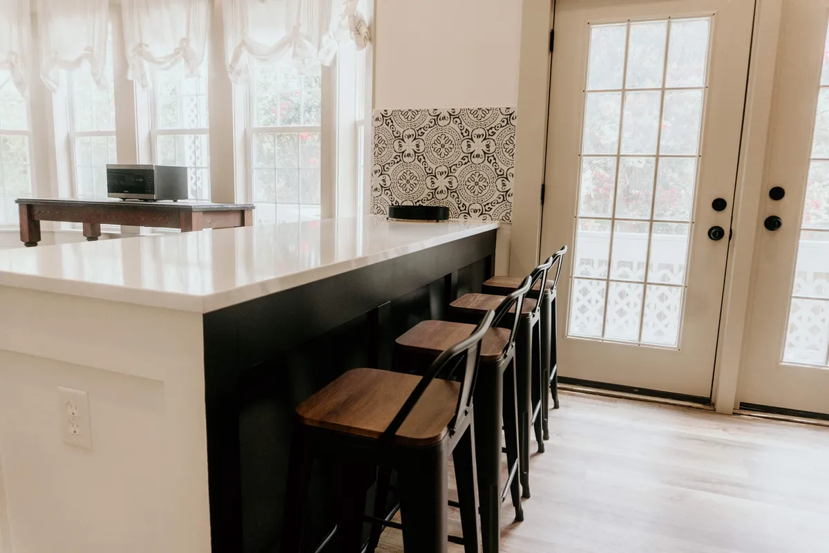 This image shows a spacious kitchen area with a prominent island, bar stools for casual dining, and a door with glass panes that visually connects the interior to the outside world. The setup encourages casual gatherings and social moments, reinforcing the home’s inviting atmosphere.