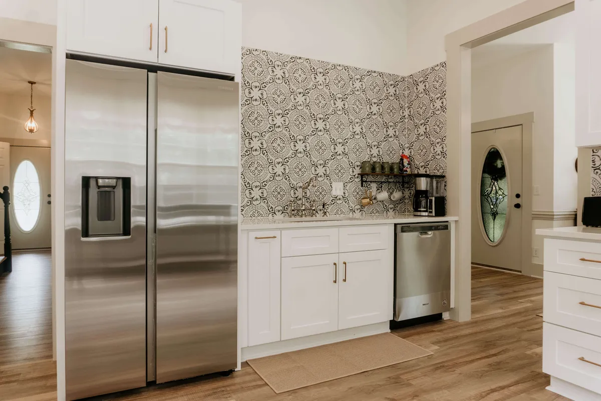 This image features a modern kitchen space with stainless steel refrigerator, decorative wall tile, and stylish kitchen cabinetry. The kitchen is bathed in natural light, with hints of cozy, communal energy—ideal for family meals or entertaining guests after a day of exploring town.