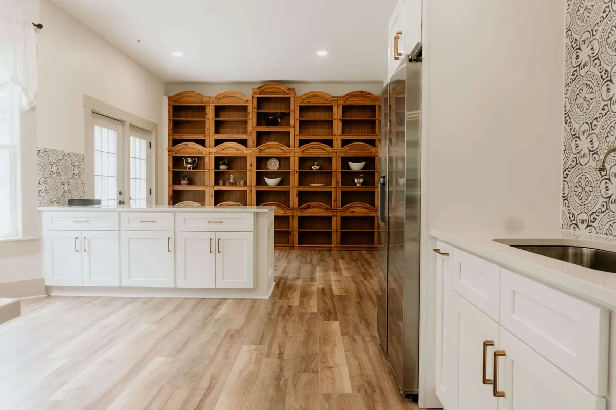 This image features a beautifully updated kitchen with a central island, wooden open shelving, and sleek stainless steel appliances. The inviting layout is perfect for cooking and entertaining, with enough space for multiple people to gather and move about comfortably.